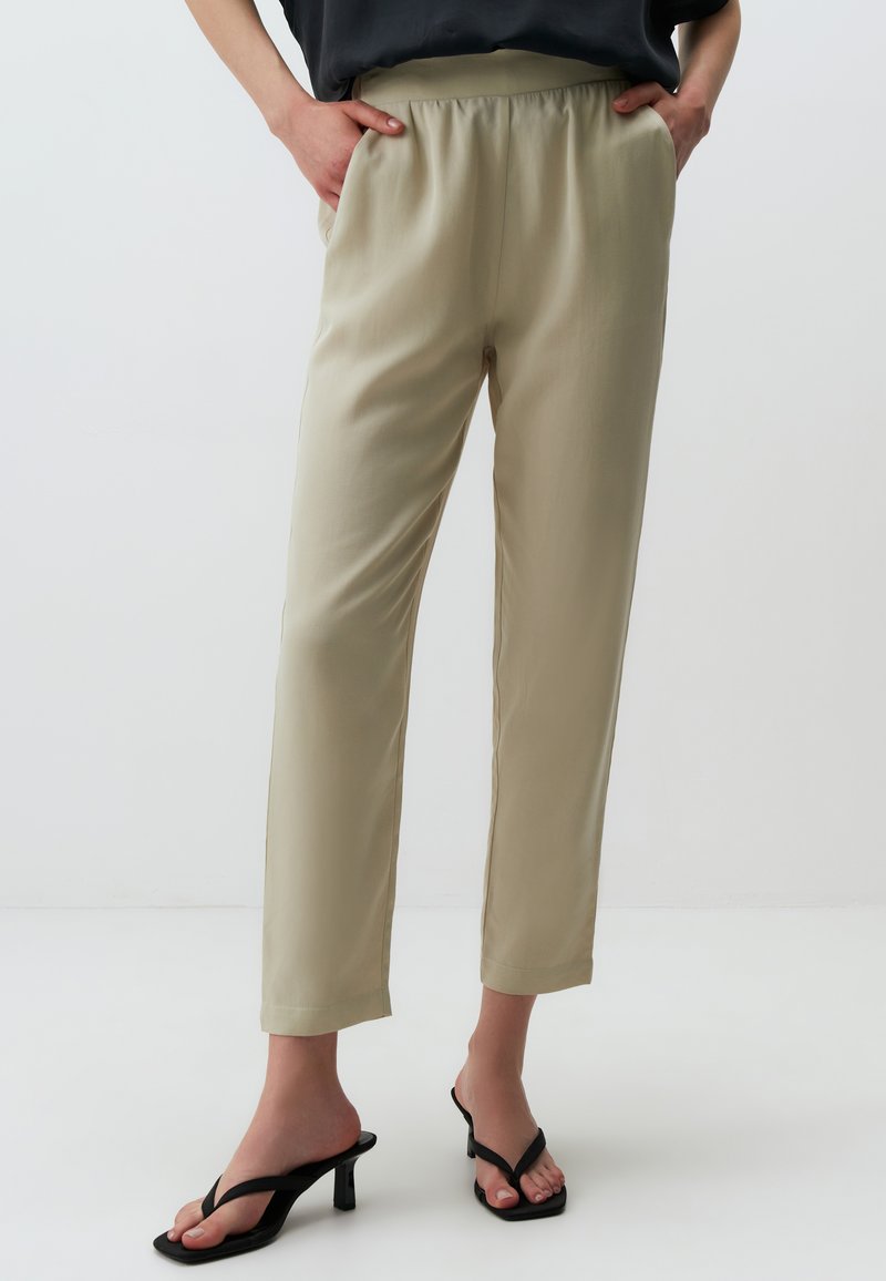 Pantaloni beige chiari a vita alta con una cintura elastica, gambe dritte e tessuto morbido. Abbinati a sandali neri con tacco.