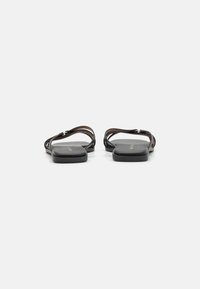 Sandales plates noires au design minimaliste, avec une tige en cuir lisse, une forme de bout carrée et des fines lanières. Semelle en caoutchouc confortable.
