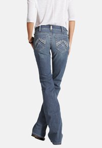 Jeans de mezclilla azul acampanados con costuras decorativas en los bolsillos traseros, que presentan una cintura de altura media y una textura suave.