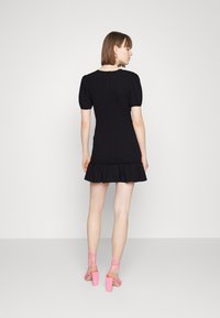 Vestido preto de mangas bufantes com barra rodada e tecido texturizado, combinado com sandálias de salto alto com tiras cor de rosa.