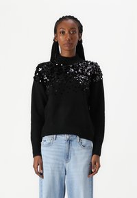 Maglione nero con embellishments di paillettes sulle spalle, realizzato in un tessuto morbido. Abbinato a jeans a gamba larga di colore blu chiaro.