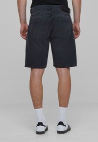Zwarte denim shorts met een rechte snit, voorzien van een tailleband, twee achterzakken en een subtiele vervaagde afwerking. Gemaakt met witte sokken en schoenen.
