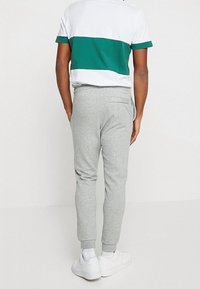 Grå sweatshirtbyxor med avsmalnande ben, elastiska muddar och en bakficka. Tillsammans med en randig t-shirt i vitt och grönt samt vita sneakers.