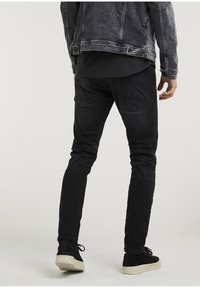 Czarne dżinsy o slim fit, zestawione z czarną koszulą i szarym dżinsowym kurtką. Obuwie ma czarny zamsz z beżową podeszwą.