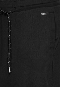 Schwarze Sweatpants aus weichem Stoff, mit elastischem Bund, verstellbarem Kordelzug mit silbernem Akzent und Seitentaschen.