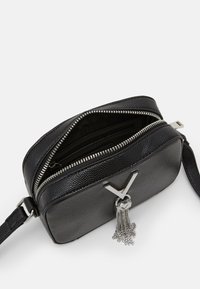 Black textured leather crossbody bag with a silver zipper, featuring a decorative tassel and a prominent "V" accent on the front.