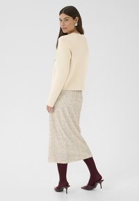 Beige pulóver, flitteres világosbarna szoknya, burgundi leggings, és burgundi magas sarkú cipők. Leengedett haj, oldalra fordítva, geometrikus fülbevalókkal.