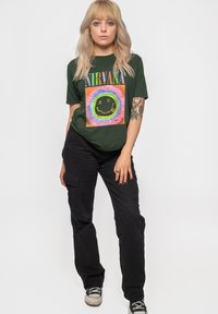 Dark green t-shirt with a colorful Nirvana graphic and smiley face, paired with black cargo pants and black sneakers.
