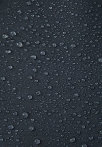 Ciemny materiał o fakturowej powierzchni, pokryty licznymi kroplami wody równomiernie rozmieszczonymi na całej powierzchni. Krople różnią się rozmiarem.