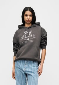 Γκρι φούτερ με κουκούλα με το γράφημα «NEW BALANCE ATHLETICS» σε λευκό, που διαθέτει τσέπη καγκουρό και άνετη εφαρμογή, συνδυασμένο με ανοιχτόχρωμο τζιν με ρίγες.