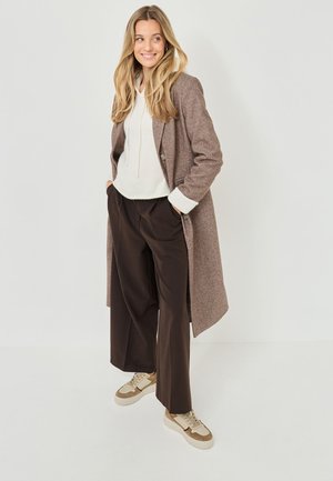 Brown wool coat over a cream hoodie, paired with dark brown trousers and beige sneakers. The coat features a single button and pockets.