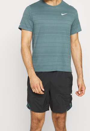 Torse d'homme portant un t-shirt Nike à manches courtes vert sarcelle et un short de sport Nike noir avec des touches subtiles de bleu et de vert.