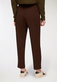 Brązowe, zwężające się spodnie z elastycznym paskiem w talii, w zestawieniu z jasnymi sneakersami z czarnymi akcentami i teksturowanym wzorem.