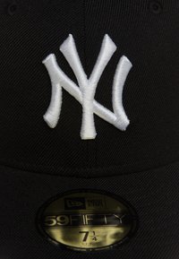 Černá čepice New Era s vyvýšeným bílým vyšitým logem New York Yankees. Má plochý kšilt a zlatou nálepku s označením velikosti 7 1/4.