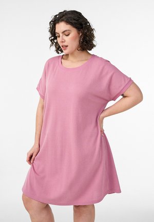 Kortsude ja lühikeste varrukatega lahtist roosa värvi põlvikuni kleiti kannav lokkis juustega naine, kes vaatab alla, üks käsi on tal puusal.