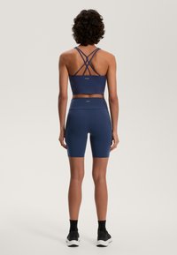 Tengerészkék sportos szett, amely egy keresztpántos sportmelltartóból és magas derekú rövidnadrágból áll, sima, rugalmas anyagból készült.