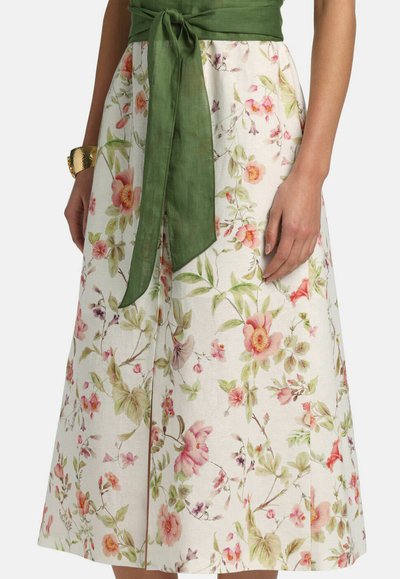 Mujer que lleva una falda midi con estampado floral con flores rosas y verdes y un fajín verde atado en la cintura, complementado con una pulsera dorada.