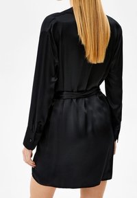 Czarna satynowa sukienka koszulowa z długimi rękawami, zapinanymi na guziki mankietami, paskiem w talii i gładką fakturą; o długości do kolan, o luźnym kroju.