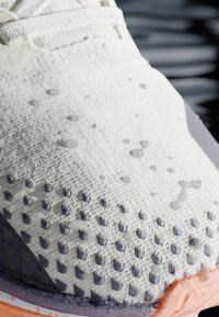 Bouts deSneakers blancs texturés avec des accents en diamant violets et des gouttes d'eau sur la surface, montrant leur résistance à l'eau.