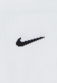 Um tecido de algodão branco apresenta um logotipo da Nike em forma de swoosh, bordado com uma textura subtil. O design é simples e minimalista.