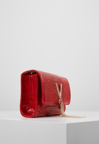 Borsa a mano in pelle rossa con stampa a coccodrillo, dotata di pattina pieghevole, tracolla in catena dorata e accento decorativo del logo. Texture liscia e forma strutturata.