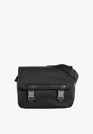 Bolso mensajero negro hecho de nailon con una textura suave. Cuenta con una solapa, dos cierres de hebilla de metal y una correa ajustable con logo.