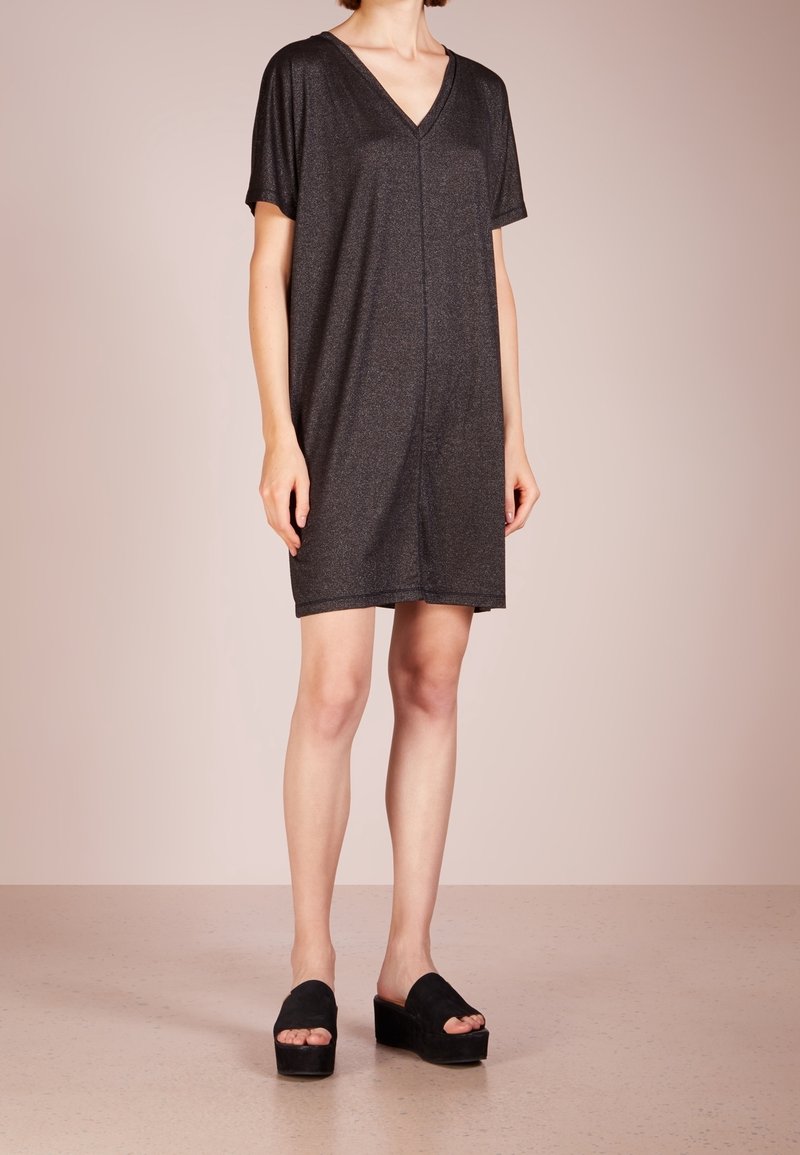 Robe noire à manches courtes et col en V en tissu texturé, à coupe ample et ourlet au milieu de la cuisse, associée à des sandales plateforme noires.