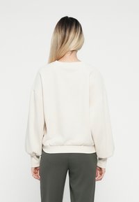 Lichtbeige sweatshirt met ronde hals en opgeblazen mouwen, elastische onderkant en een zachte textuur, gecombineerd met olijfgroene broek.