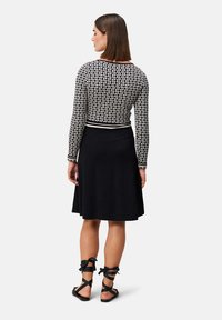 Zwarte jurk met een uitlopende rok, gecombineerd met een aansluitend, gestreept langetermijn top. Sandalen hebben zwarte banden met strikjes rond de enkels.