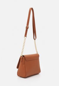 Brązowa skórzana torba na ramię o wyraźnym kształcie, z klapą z przodu i złotym detalem łańcuszka. Ma teksturowane wykończenie.