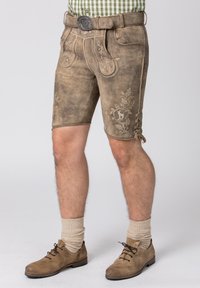 Bruine leren shorts met decoratieve borduursels en metalen accenten. Voorzien van zijveters en een riem, gecombineerd met beige sokken en bruine schoenen.