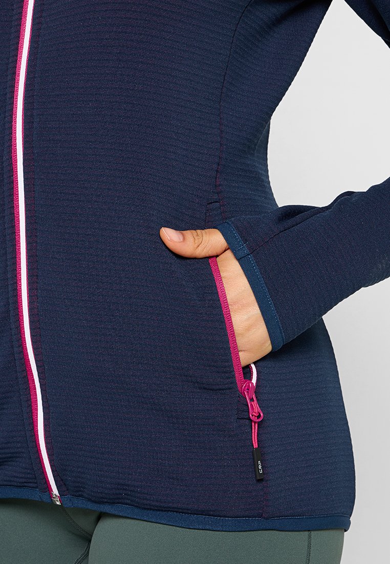 Veste de sport texturée bleu marine avec une fermeture éclair et des accents roses, dotée d'une poche latérale et de trous pour les pouces pour des manches allongées.