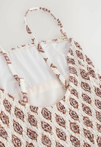Rochie albă fără mâneci, cu un model floral intricate de culoare maro, textură pliată, bretele ajustabile cu model și căptușeală interioară netedă.