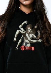 Sudadera negra con un diseño gráfico de una figura con múltiples brazos. "Grimey" está impreso en letras rojas y en negrita en la parte inferior.