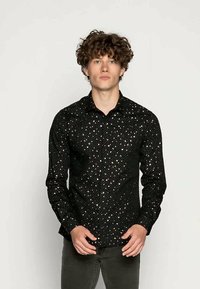 Camicia nera con bottoni, caratterizzata da un motivo a pois con accenti metallici, maniche lunghe e colletto classico. Tessuto dalla texture liscia.
