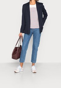 Blazer navy, camicia a righe bianca e marrone, jeans dritti blu, sneakers azzurre chiare con dettagli rosa e borsa bordeaux.
