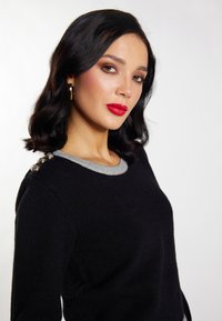 Pulover negru cu guler gri, având nasturi decorativi pe umăr. Textură moale, croială ajustată și mâneci lungi.