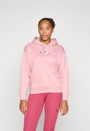 Lys rosa hettegenser med frontlomme, snorhette og en logo sentrert på brystet. Båret sammen med rosa leggings med en liten logo.