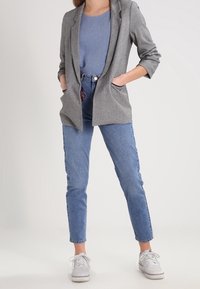 Szary, teksturowany żakiet z klapami, noszony na niebieskiej koszuli. W zestawie z jasnoniebieskimi dżinsami i białymi trampkami, w luźnym kroju.