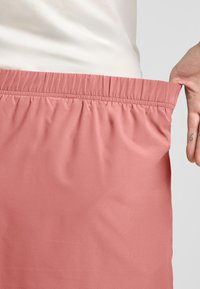 Gonna rosa con cintura elastica in un tessuto morbido e leggero, tenuta per la cintura per mostrare i dettagli di texture e vestibilità.