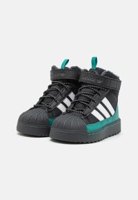 Botas negras y verde azulado de media altura con tres rayas blancas, puntera de goma texturizada, cordones y detalles de costura en contraste.