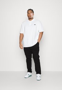 Hvit polo skjorte med en liten logo, kombinert med svarte bukser og hvite sneakers med teal-detaljer. Glatt stoff, uformet passform.