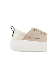 Sneaker in pelle beige con accenti testurizzati bianco sporco, caratterizzato da una suola bianca, forma arrotondata e nome del marchio impresso di lato.