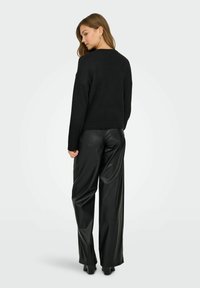 Maglione nero a maglia con scollatura rotonda e maniche lunghe, abbinato a pantaloni wide-leg neri in ecopelle a vita alta. Texture liscia.