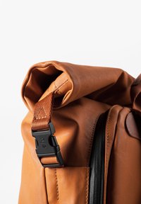 Zaino marrone a roll-top con finitura testurizzata, fibbia in hardware nero e tracolla a contrasto. Include una zip laterale e una parte superiore pieghevole.