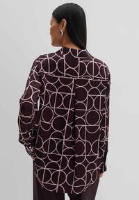 Long-sleeve shirt in dark burgundy with a geometric pink circle pattern, featuring a back yoke and buttoned cuffs for adjustable fit.