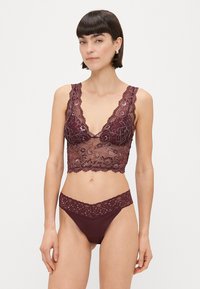 Bordo čipkasti bralette s cvjetnim uzorcima i valovitim rubovima, u kombinaciji s odgovarajućim slip gaćicama s čipkastim rubovima. Glatka tekstura tkanine.
