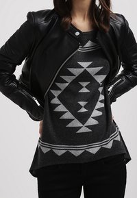 Veste de motard en cuir noir sur un pull à motif gris arborant des formes triangulaires et des losanges, avec un bas légèrement évasé et des manches longues.
