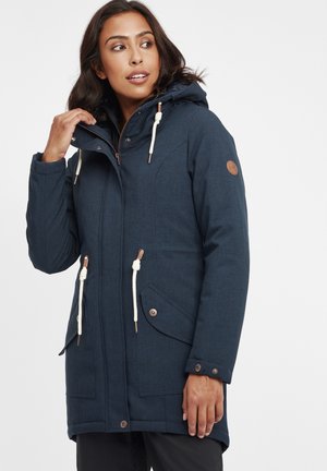 Parka blu navy con cappuccio in tessuto texturizzato, dotata di lacci, due tasche laterali, bottoni metallici e una patch con logo sulla manica.