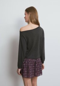 Suéter gris oscuro con diseño de hombros descubiertos, combinado con una falda fluida y estampada en tonos burdeos profundos y púrpura. Textura suave.